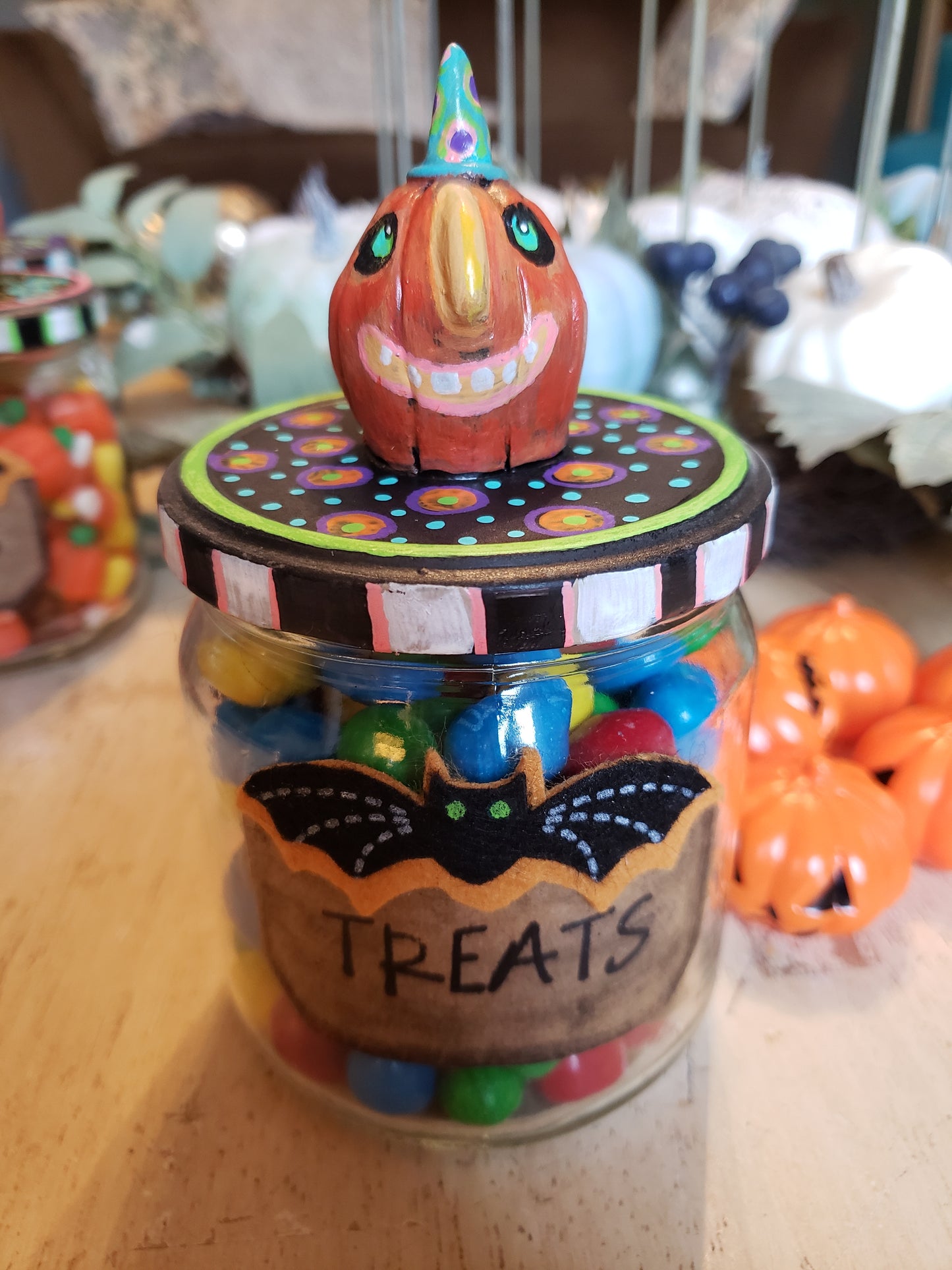 Decorative Halloween candy jar with colorful candies and a pumpkin design on a wooden surface.