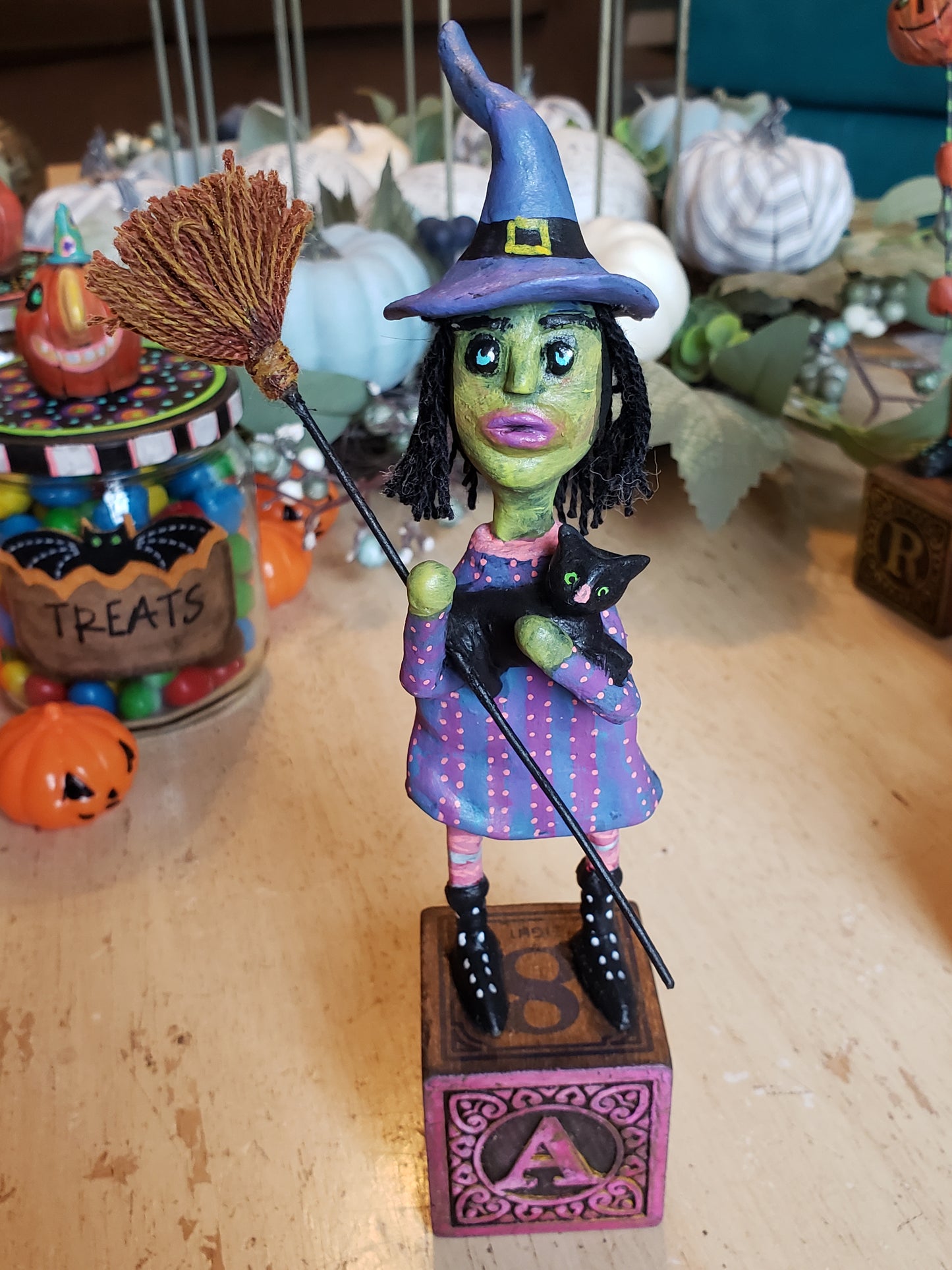 Colorful Halloween-themed figurine of a witch with a black cat on a broomstick. Paper clay figurine