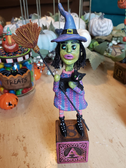 Colorful Halloween-themed figurine of a witch with a black cat on a broomstick. Paper clay figurine