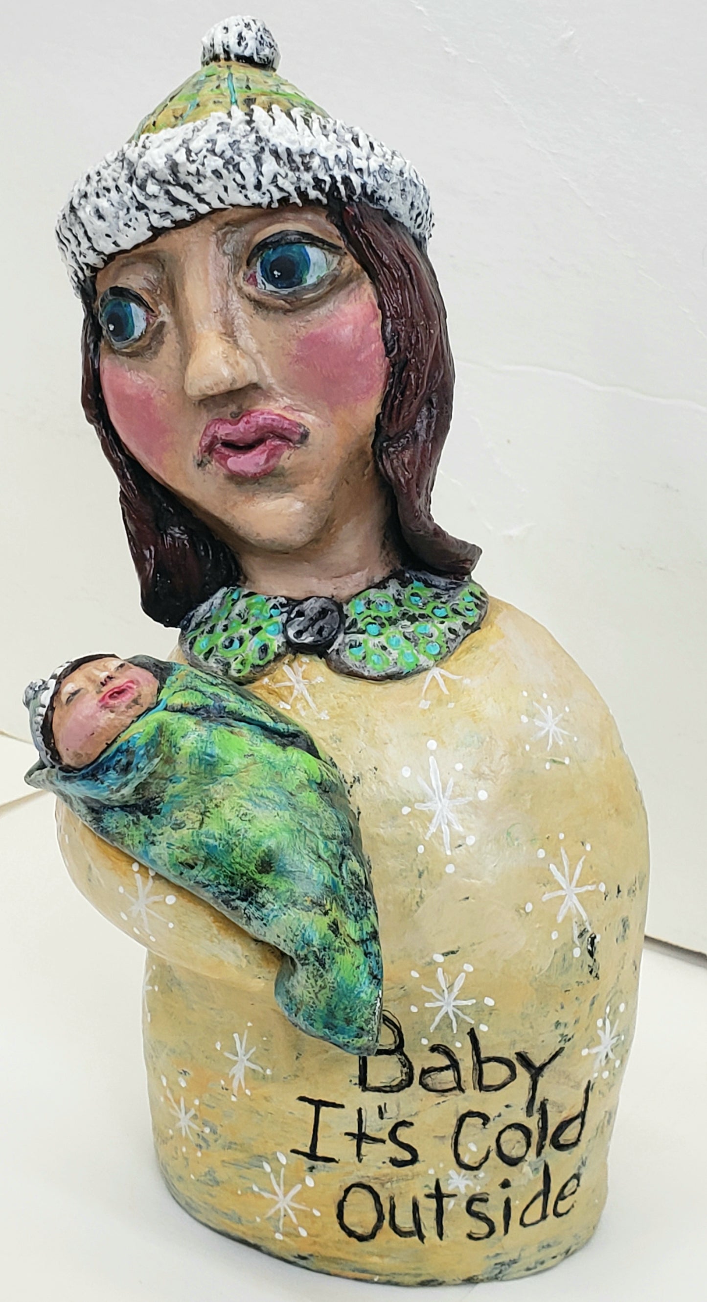 Decorative paper clay figurine of a woman holding a baby with text 'Baby It's Cold Outside' standing Christmas decoration