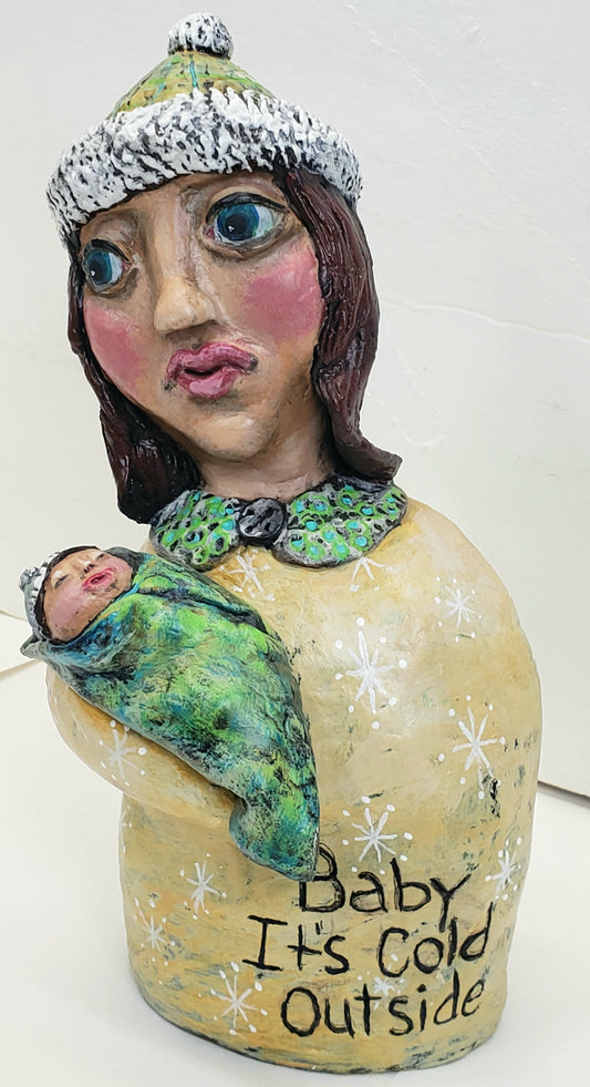 Decorative paper clay figurine of a woman holding a baby with text 'Baby It's Cold Outside' standing Christmas decoration