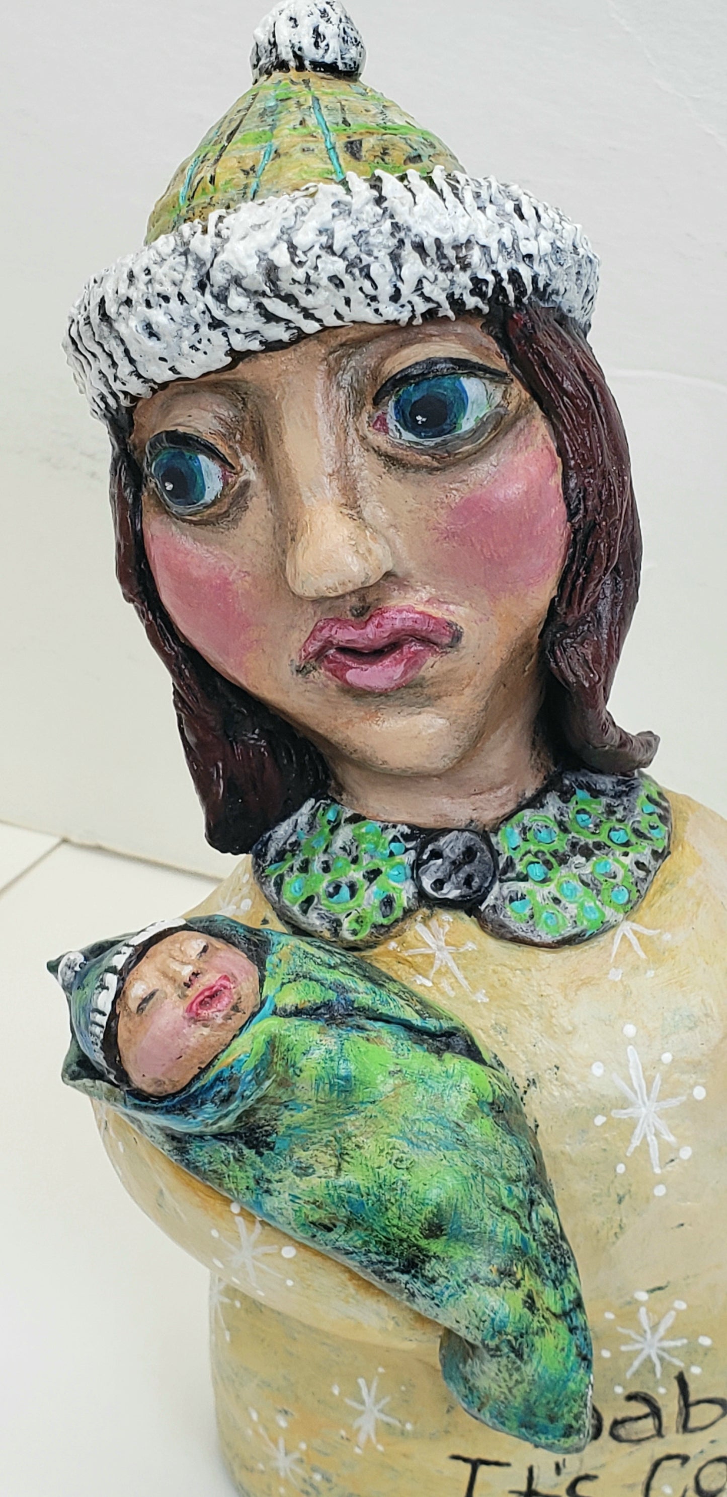 Decorative paper clay figurine of a woman holding a baby with text 'Baby It's Cold Outside' standing Christmas decoration